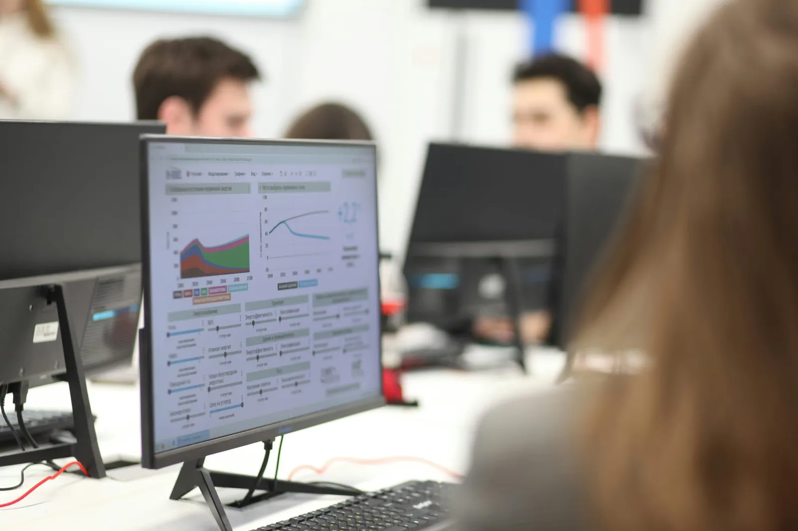 Analyst viewing a dashboard of charts and scenario sliders on a monitor in a shared office