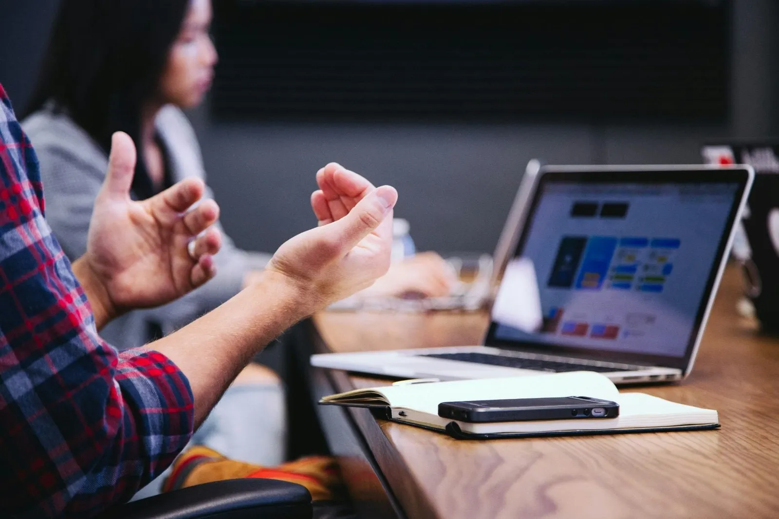 Person gesturing at a meeting table beside a laptop and notebook, used for the RPO firm's AI recruitment customer story.